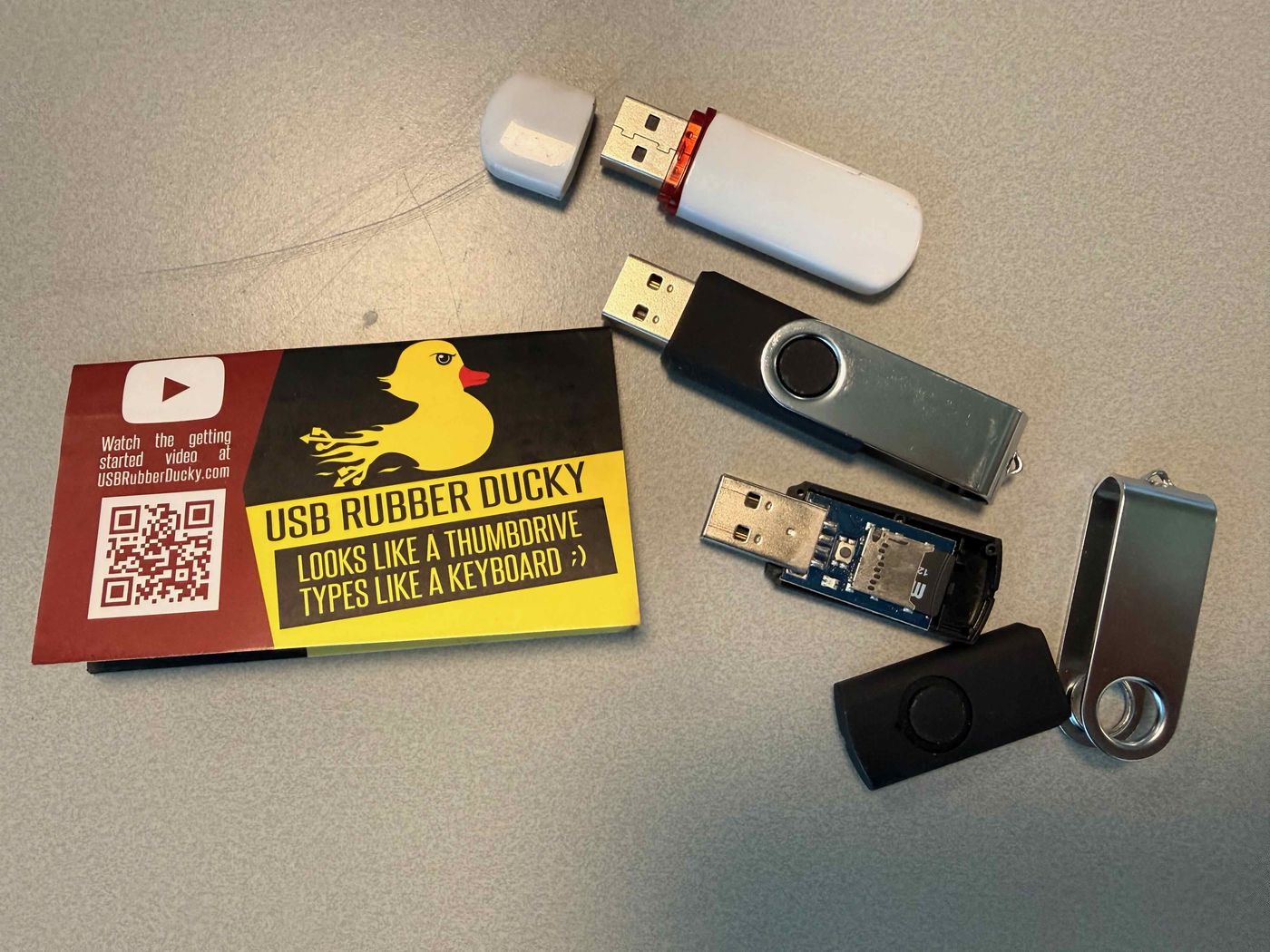 USB Rubber Ducky met de microSD-kaart zichtbaar, naast lookalike USB-sticks en het Rubber Ducky-kaartje